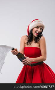 Young celebrating woman christmas santa hat and dress. Beautiful model portrait isolated over studio background opening champagne bottle.