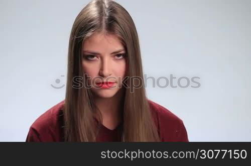 Young charming brunette woman with amazing long hair looking at the camera viciouslyon white. Stunning displeased girl with deep brown eyes staring with murderous look.