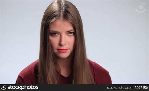 Young charming brunette woman with amazing long hair looking at the camera viciouslyon white. Stunning displeased girl with deep brown eyes staring with murderous look.