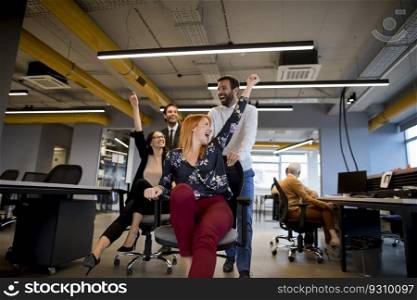 Young cheerful business people in smart casual wear having fun while racing on office chairs and smiling