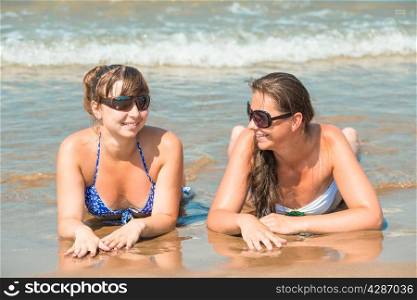 Young cheerful girlfriends lie on the the sandy shore