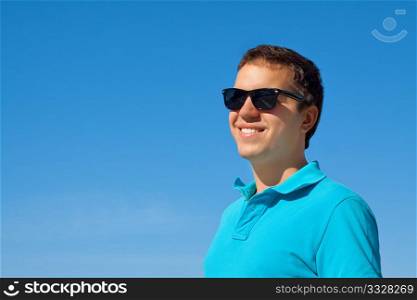 young cheerful man in sunglasses against blue sky