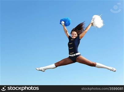 Young cheerleader in green costume jumping against blue sky