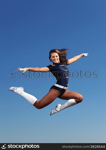 Young cheerleader in green costume jumping against blue sky