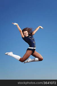 Young cheerleader in green costume jumping against blue sky