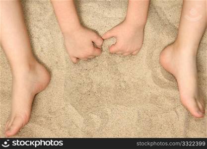 Young child&acute;s hands and feet in sand.