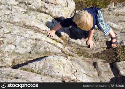 Young child, climbing a big rock on using his hands and feet