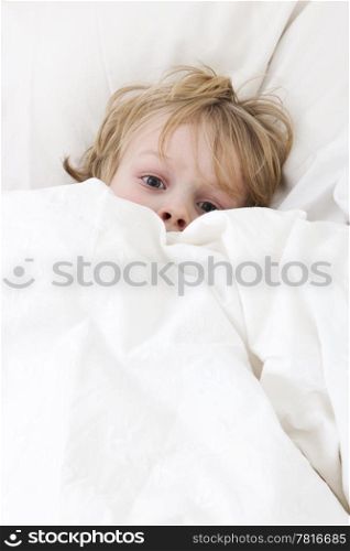 Young child, lying awake in his bed, with his eyes wide open, covering himself up, scared from the nightmare he just had