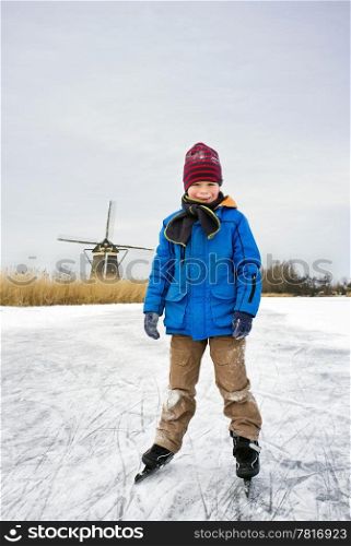 Young child, skating and smiling into the camera on the ice of a frozen canal in typical Dutch scenery