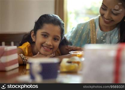 Young child smiling in front while resting her head on the table