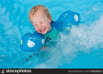 Young child swimming with arm bands and being splashed