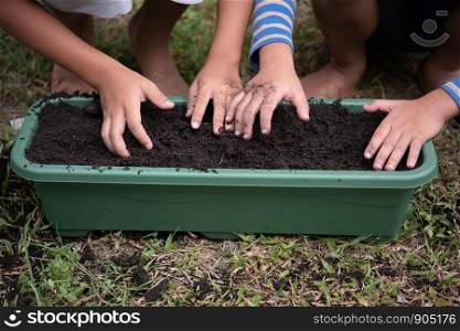 young children planting seeds in garden.Hand holding seed and black soil in pot