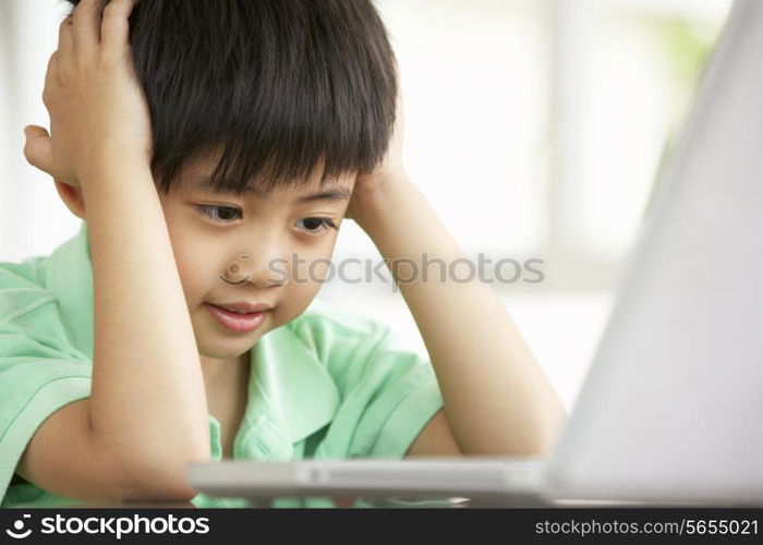 Young Chinese Boy Sitting At Desk Using Laptop At Home