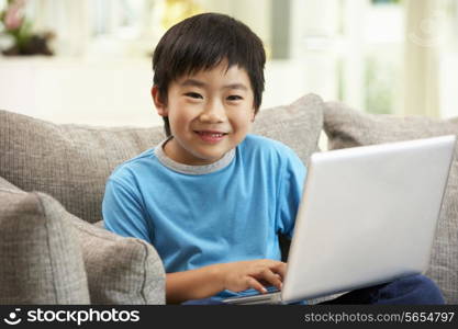 Young Chinese Boy Using Laptop Whilst Sitting On Sofa At Home