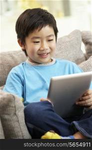 Young Chinese Boy Using Tablet Computer Whilst Sitting On Sofa At Home