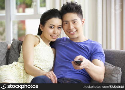 Young Chinese Couple Sitting And Watching TV On Sofa At Home