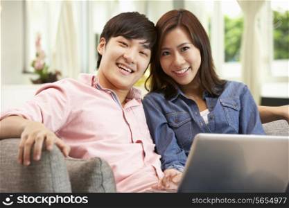 Young Chinese Couple Using Laptop Whilst Relaxing On Sofa At Home