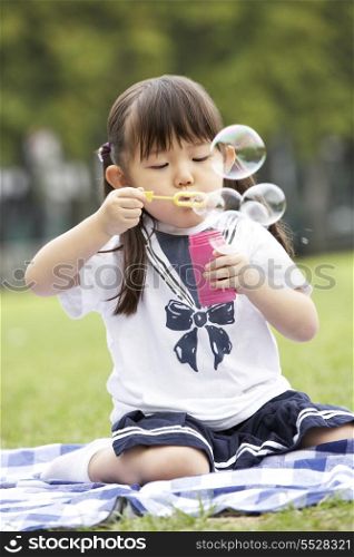 Young Chinese Girl In Park Blowing Bubbles