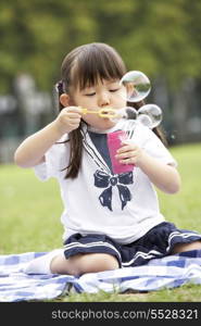 Young Chinese Girl In Park Blowing Bubbles