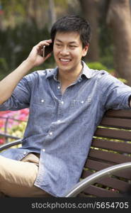 Young Chinese Man Relaxing On Park Bench Talking On Mobile Phone