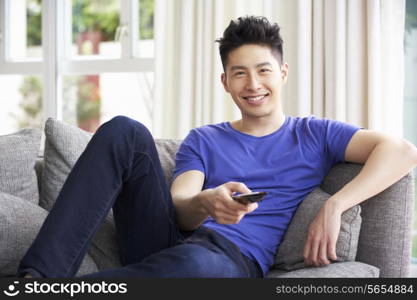 Young Chinese Man Sitting And Watching TV On Sofa At Home