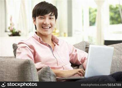 Young Chinese Man Using Laptop Whilst Relaxing On Sofa At Home