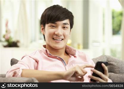 Young Chinese Man Using Mobile Phone On Sofa At Home