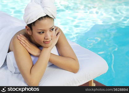 Young Chinese woman lying by swimming pool