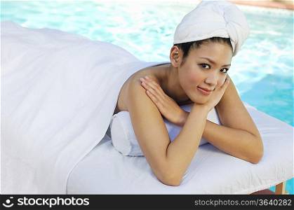 Young Chinese woman lying under towel by swimming pool, portrait