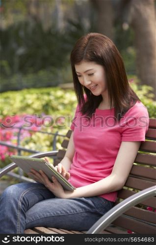 Young Chinese Woman Using Digital Tablet Whilst Relaxing On Park Bench