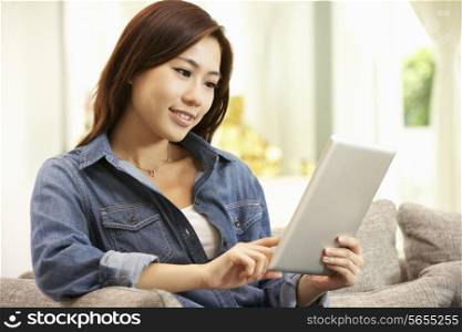 Young Chinese Woman Using Digital Tablet Whilst Relaxing On Sofa At Home