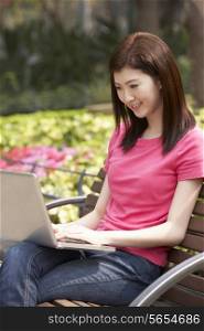 Young Chinese Woman Using Laptop Whilst Relaxing On Park Bench