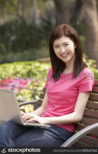 Young Chinese Woman Using Laptop Whilst Relaxing On Park Bench