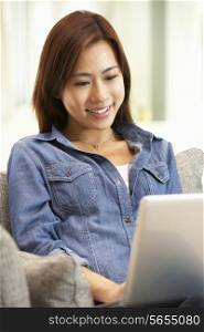 Young Chinese Woman Using Laptop Whilst Relaxing On Sofa At Home