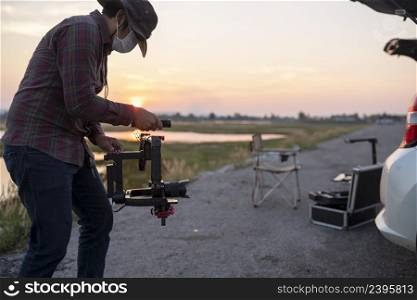 Young cinematographer using gimbal stabilizer shooting video footage for content creator of him on the location outdoor.