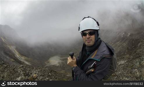 Young climber man walking with black coat and helmet using trekking pole alone by the crater of Guagua Pichincha volcano on a cloudy day. Young climber man walking with black coat and helmet using trekking pole alone by the crater of Guagua Pichincha volcano