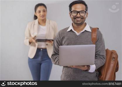 Young co-workers man and woman standing with laptop and digital tablet in office