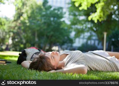 Young college student lying down on grass at campus lawn