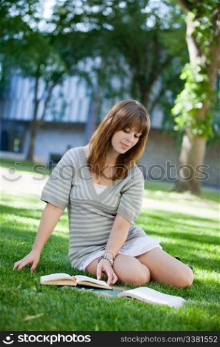 Young college student reading book on campus lawn
