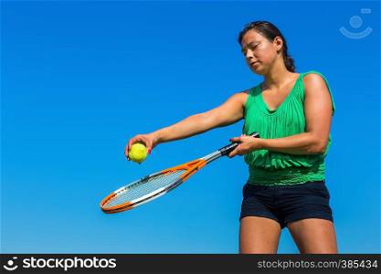 Young colombian woman holding tennis racket and ball against blue sky
