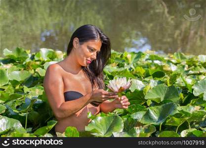 Young colombian woman holding white water lily flower in european pond