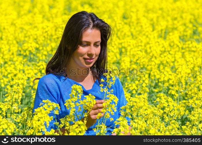 Young colombian woman looking at flower in blooming yellow rapeseed field