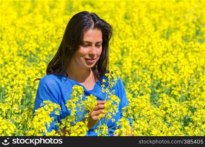 Young colombian woman looking at flower in blooming yellow rapeseed field