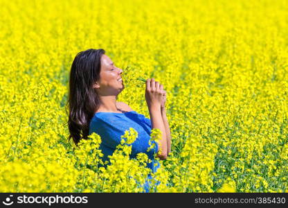 Young colombian woman smelling yellow flowers in agricultural rapeseed field