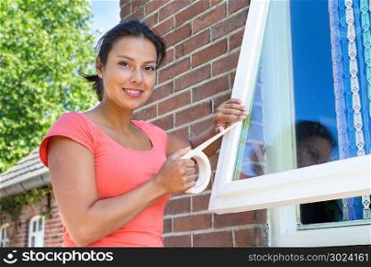 Young colombian woman sticking adhesive tape on window glass