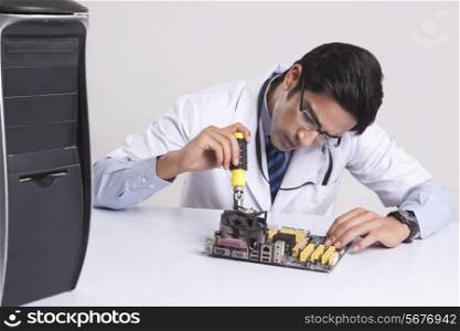 Young computer technician working on mother board against gray background