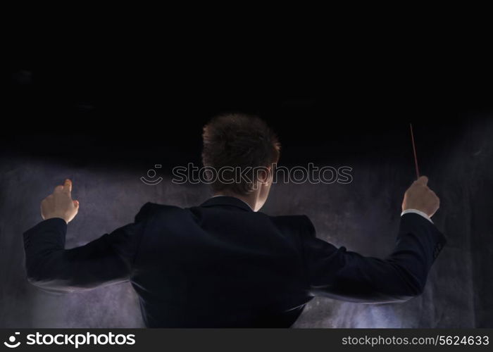 Young conductor with baton raised at a performance, rear view