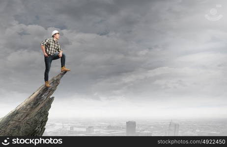 Young confident builder standing on rock edge high above city. Conquering the top