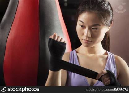 Young confident female boxer wrapper her wrists in the gym