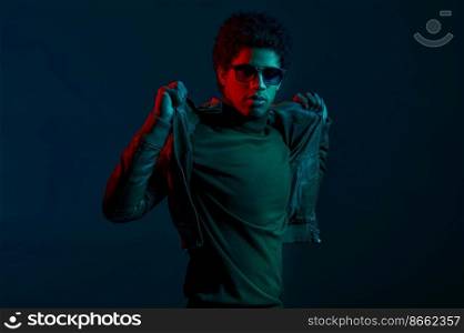 Young confident stylish man model puts on leather jacket over dark background. Young confident man puts on jacket over dark background